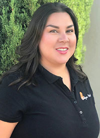 Woman standing outdoors, smiling and wearing a polo shirt with a logo.