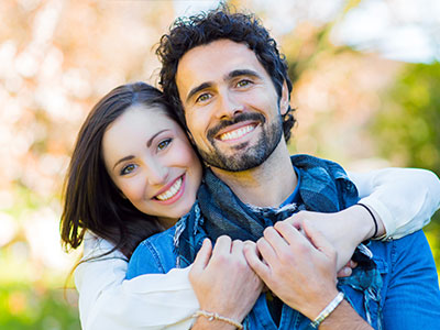 A man and a woman in a warm embrace, smiling at the camera.