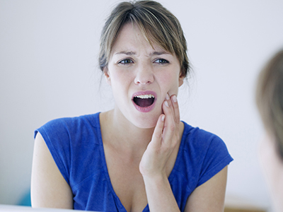 The image depicts a woman with her mouth open, showing teeth and holding her hand to her face. She appears distressed or concerned, looking directly at the camera with a focused expression.