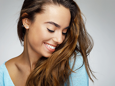 A woman with long brown hair, wearing a light blue top, smiling gently and looking to her left.