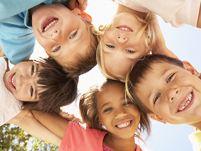 A group of children, some smiling and posing for a photo, with the sun shining brightly in the background.