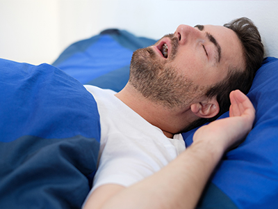 A man is lying in bed, with his head resting on a blue pillow, seemingly sleeping or resting.