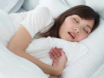 A woman sleeping peacefully in a bed with her eyes closed, wearing a white shirt and a necklace.